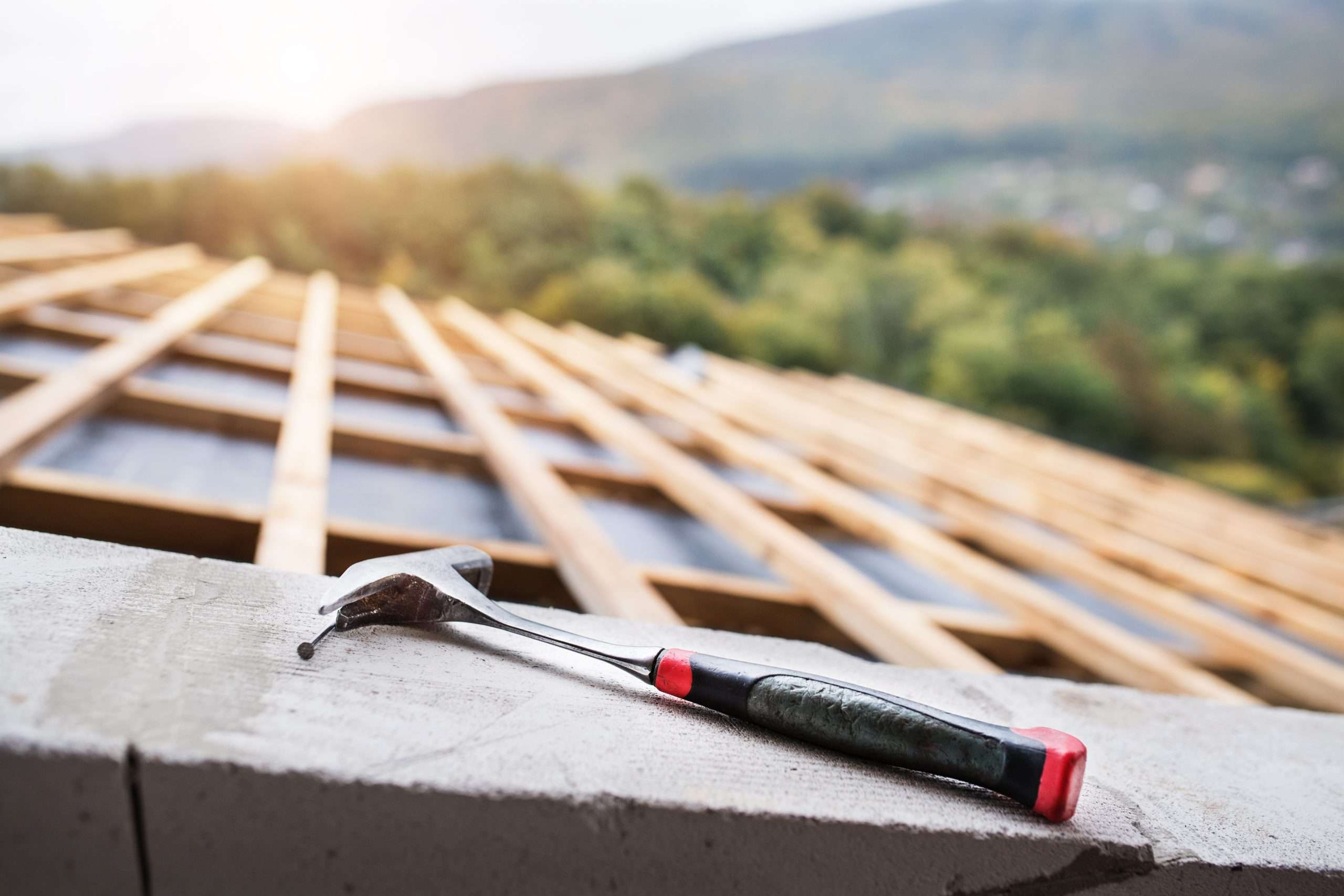 A construction worker using a hammer on a roof at a job site.